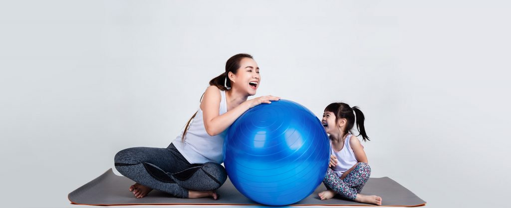 Seorang ibu yang berolahraga dengan bola yoga bersama anaknya
